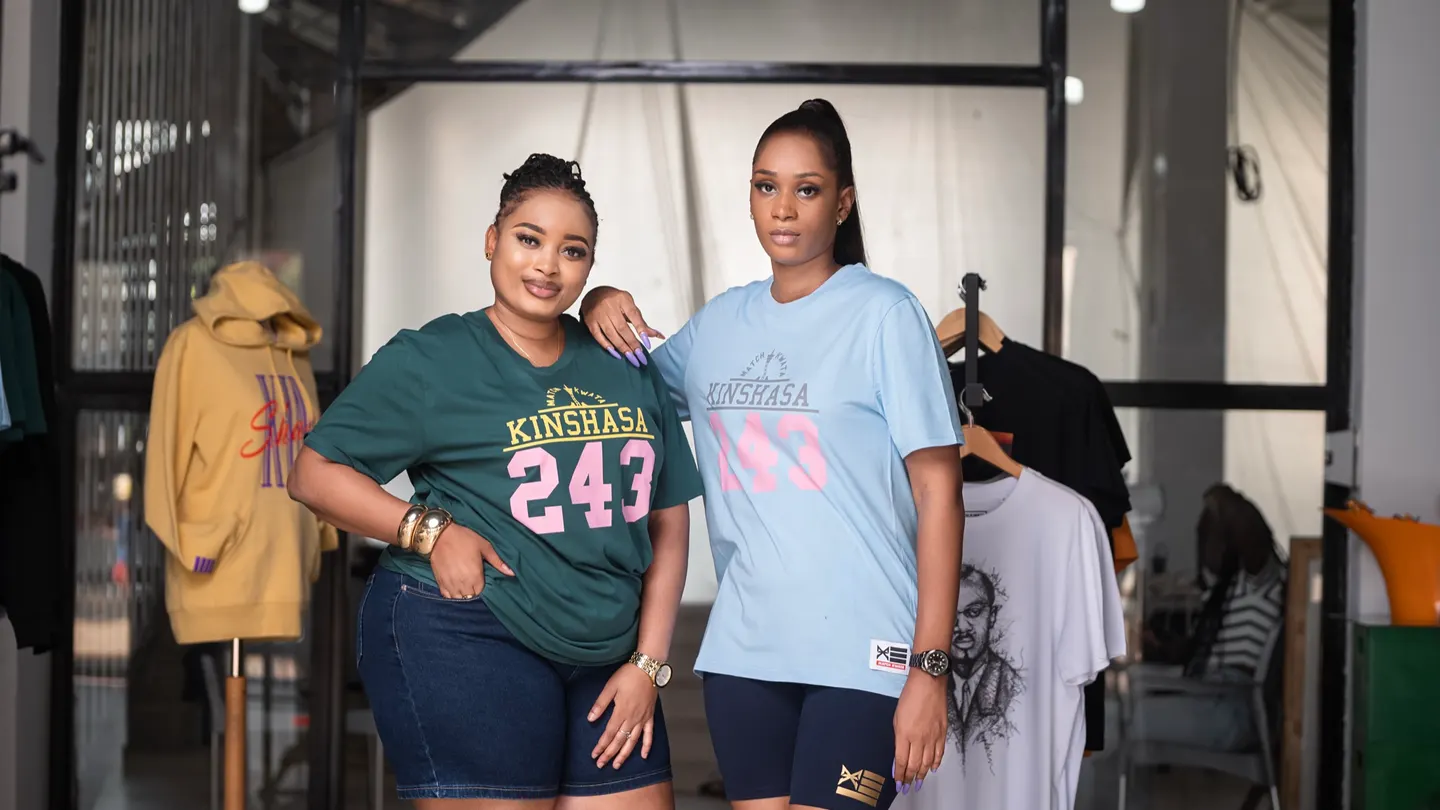 Deux clientes en t-shirts Match Kwata Kinshasa 243, vert et bleu ciel, dans la boutique de Kinshasa